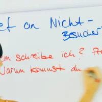Eine Frau schreibt etwas auf ein großes Blatt Papier, das an der Wand hängt.