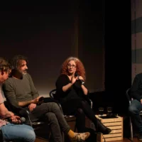 Four people sit in a slight semi-circle on the stage and discuss with each other.