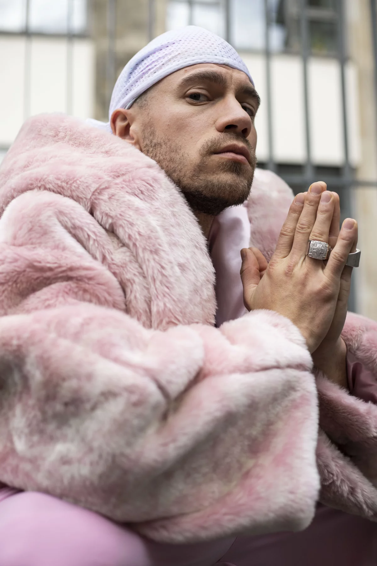Performer ist wie Rapper gekleidet, jedoch in den Farben weiß und pink mit pinker Pelzjacke und pinker Hose. Er trägt ein weißes Kopftuch und große silberne Ringe.