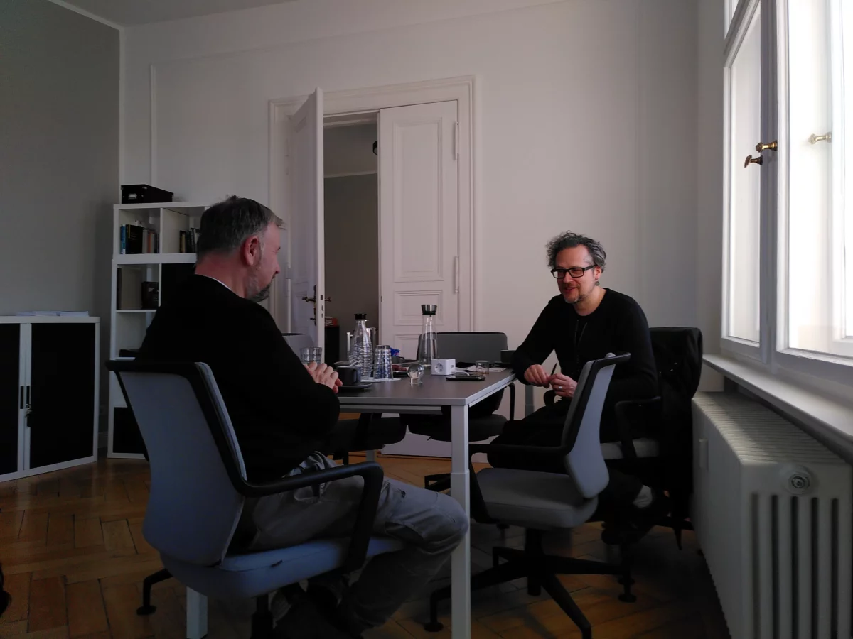 Holger Bergmann und Falk Schreiber sitzen sich an einem Tisch gegenüber.