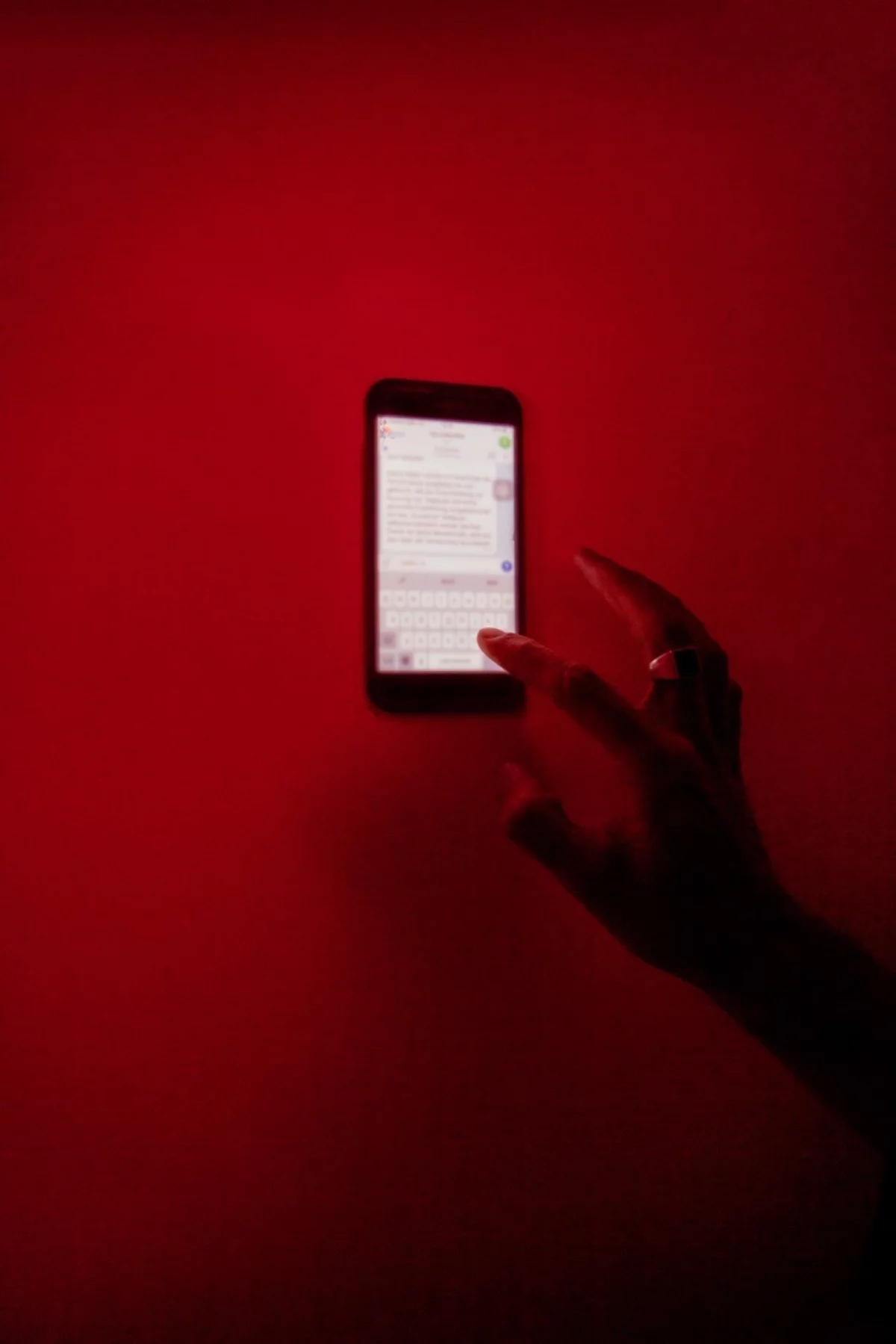 Vor einem roten Hintergrund befindet sich ein Smartphone, auf dem ein Messengerdienst geöffnet ist. Eine Hand tippt darauf eine Nachricht ein.
