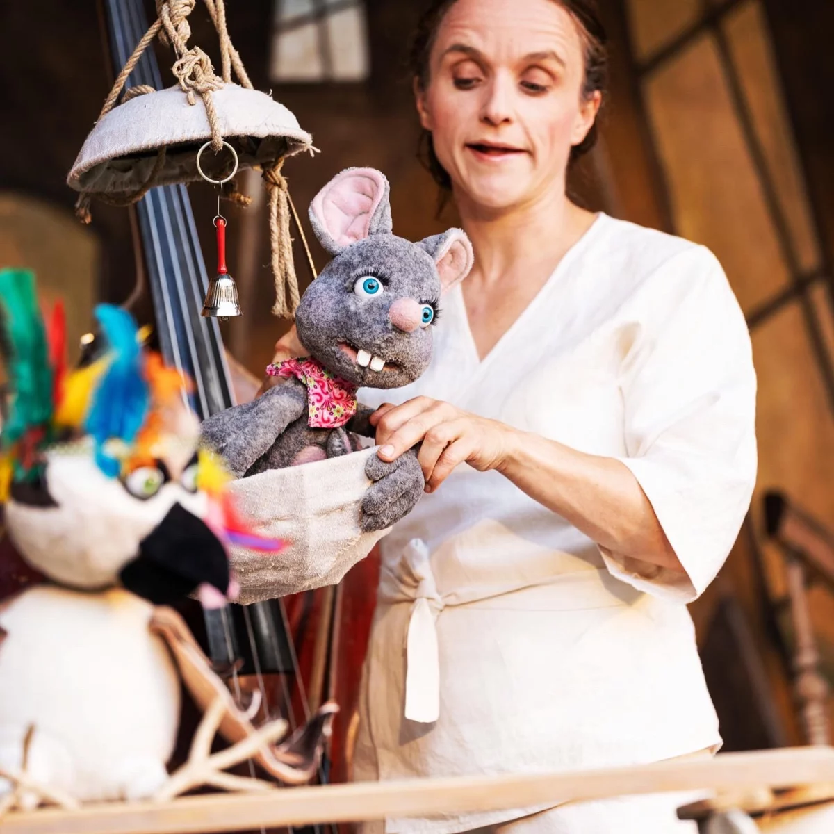 A puppeteer is operating a gray mouse puppet that is peeking out of a bowl in front of her.