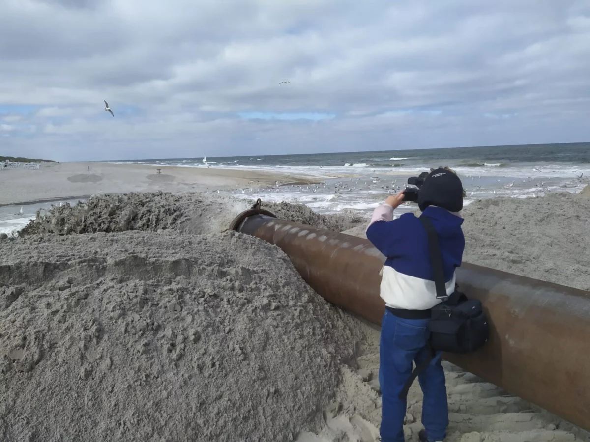 Aus einem dicken Rohr wird Sand an den Strand von Sylt gespült - im Hintergrund die Nordsee