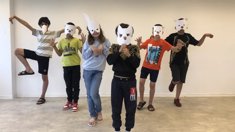 A group of children with self-made paper masks perform a choreography.