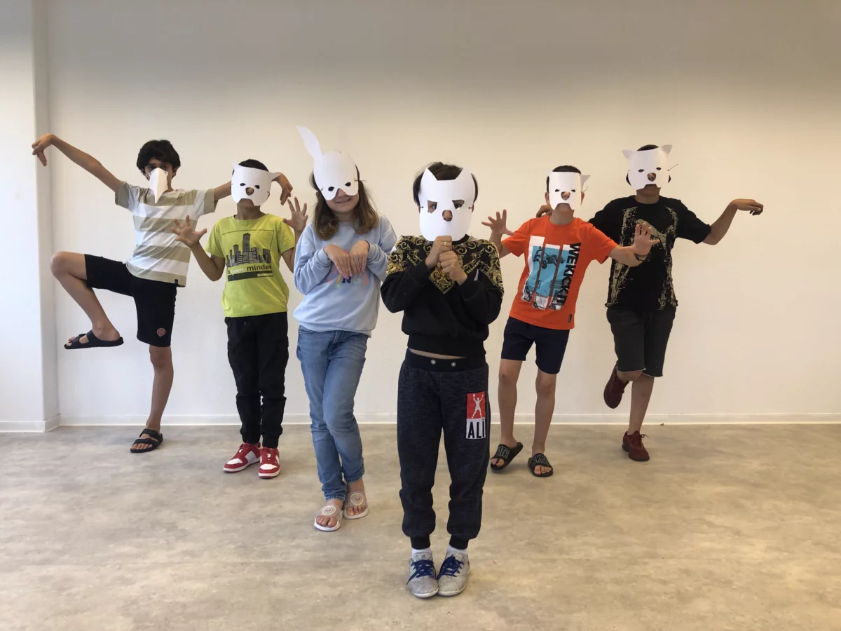 A group of children with self-made paper masks perform a choreography.