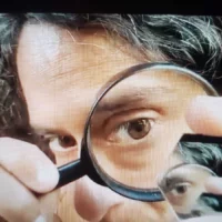 A person looks through a magnifying glass at a small piece of mirror.