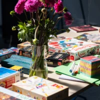 You can see a bouquet of flowers in a vase surrounded by board games and other board games as well as work materials.