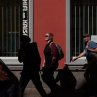 Vier Personen laufen mit Gepäck an einer roten Häuserwand vorbei.