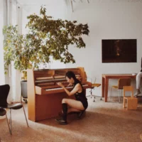 A woman sits in front of a piano and plays on it.