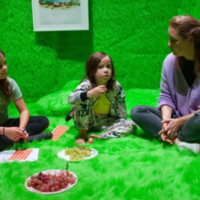 Eine Person sitzt mit zwei Kindern einem Raum voller grünem Plüsch.