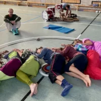In a sports hall, several people are lying on the floor and touching each other.