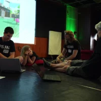 Vier Personen sitzen auf dem Boden zusammen und befinden sich mit ihren Laptops in einer Arbeitssituation.