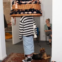 Eine Person steht mit ihrem Hund unter einer Kunstinstallation, die aussieht als wär sie ein großer Hut.