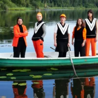Five people are standing in a boat on a lake.
