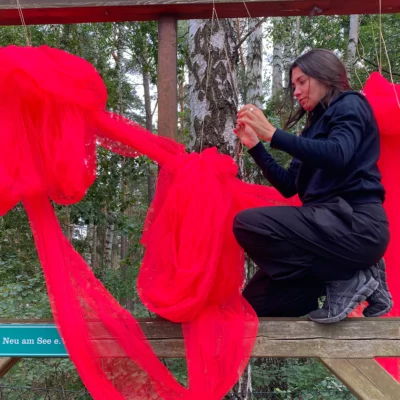 A woman attaches a red cloth to a wooden beam.