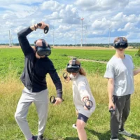 Three people with VR glasses pose in front of a field.