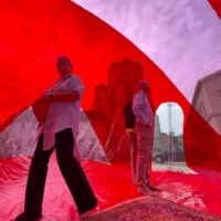 Zei Personen befinden sich in einer Installation aus roten langen Plastikplanen, die um sie herum schweben.