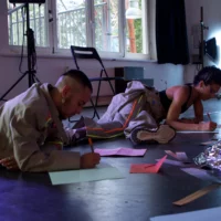 Two people are lying on a floor and writing something on pieces of paper.