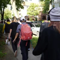 Eine Personengruppe läuft auf einem Fußweg im öffentlichen Raum mit Kopfhörern hintereinanderher.