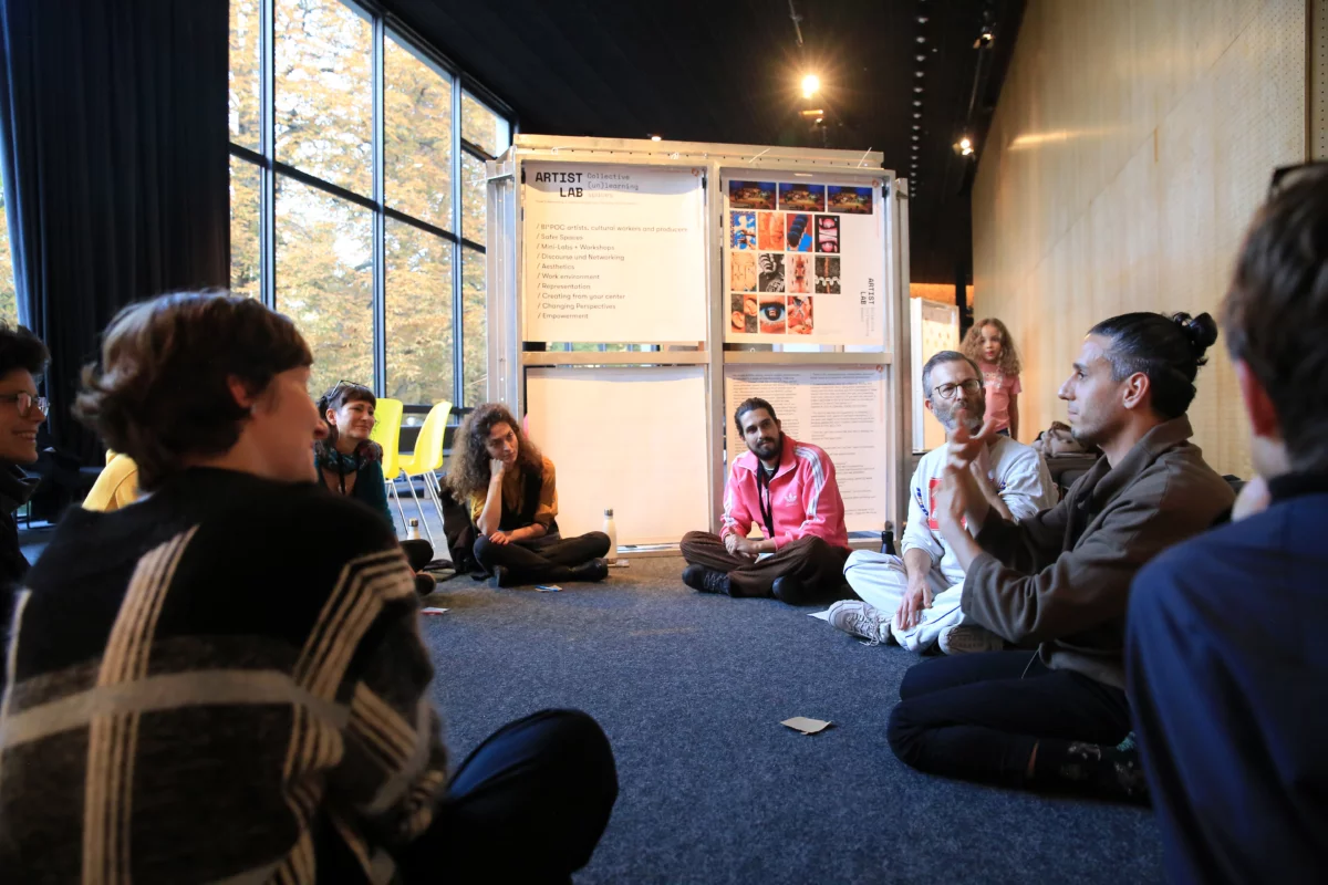 A group of people sits between exhibition walls with posters and graphics and discuss with each other.