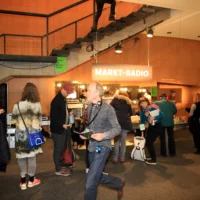 People line up in the foyer of the Berliner Festpiele at the market's headphone counter. An illuminated sign reading "MARKET RADIO" is emblazoned above their heads.