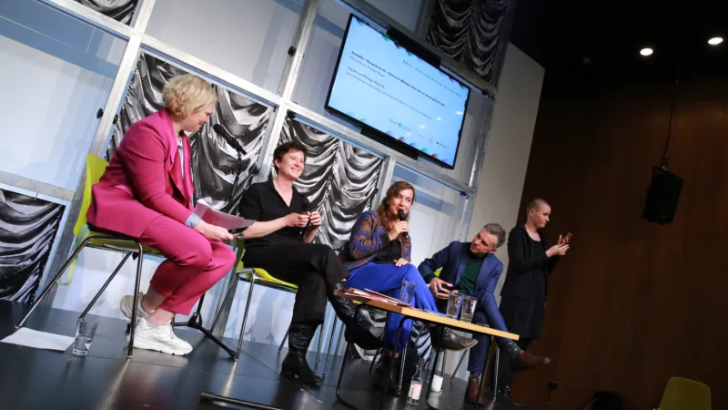 The picture shows four people sitting next to each other on stage. They are discussing with each other as part of a panel discussion.