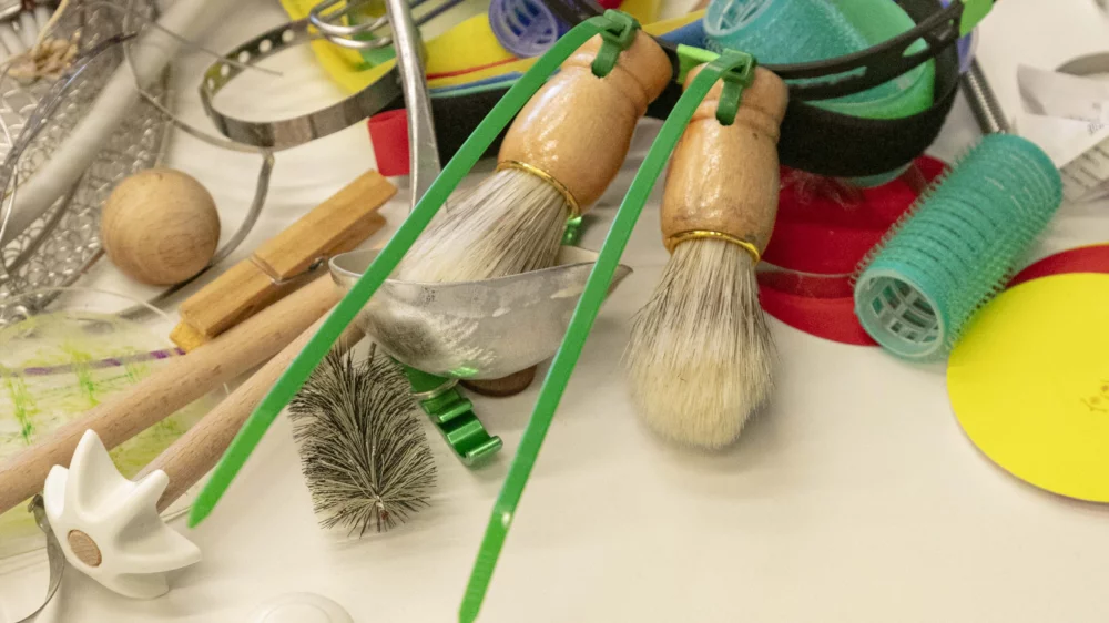 A colorful collection of things on a table: shaving brushes, cooking utensils, hair curlers, small cable ties, clothespins.