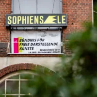 Unterhalb der Leuchttafel mit der Wortmarke der Sophiensaele im Hof ist ein Banner der Veranstaltung mit dem Aufdruck "Bündnis für Freie Darstellende Künste. Bundesforum 2019, 3.9.2019, Sophiensaele Berlin" angebracht.