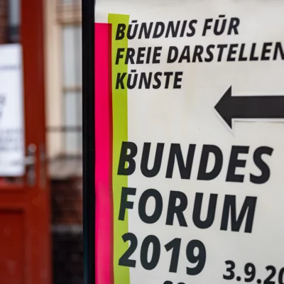 Image of the poster of the event with the inscription "Bündnis für Freie Darstellende Künste - Bundesforum 2019, 3.9.2019". An arrow points to the entrance of the Sophiensaele visible in the background.