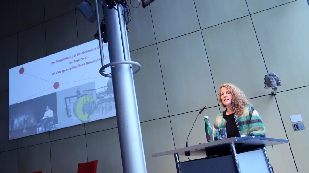 Portrait von Dr. Hilke Marit Berger am Redner*innenpult während des Vortrags. Im Hintergrund ist eine illustrierende Projektion zu sehen.