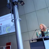 Portrait of Dr. Hilke Marit Berger at the lectern during the lecture. An illustrative projection can be seen in the background.