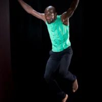 Close-up of a dancer jumping, legs slightly bent, hands stretched far up. His face is concentrated.