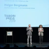 Annemie Vanackere und Holger Bergmann begrüßen das Publikum auf der Bühne bei der Eröffnung der Preisverleihung.