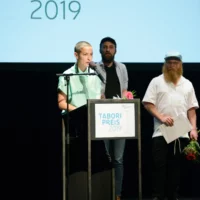 The performers of machina eX at the award ceremony on the stage of HAU 1. The director Anna Sina Fries stands at the microphone of the lectern for her acceptance speech.