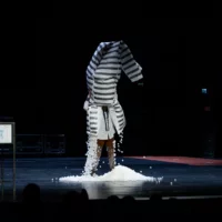 Künstlerischer Beitrag auf der Bühne: Ein Performer streift sich ein großes, gestreiftes Kostüm über den Kopf, während gleichzeitig Styroporkugeln daraus rieseln.
