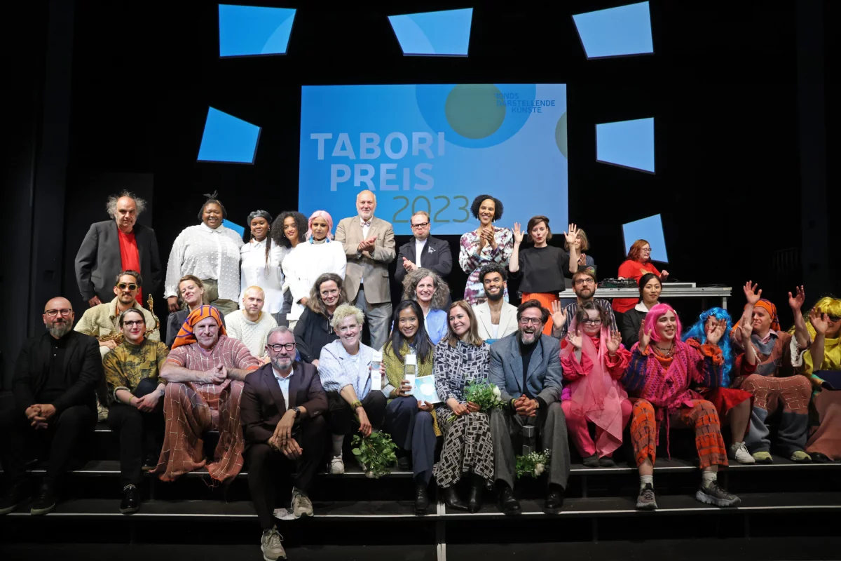 Gruppenfoto aller Beteiligten der Tabori Preisverleihung 2023 auf der Bühne des HAU 1. Im Zentrum die glücklichen Gewinner*innen und Ausgezeichneten.