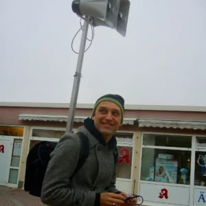 Foto von Torsten Michaelsen mit Rucksack und Mütze vor einer Apotheke