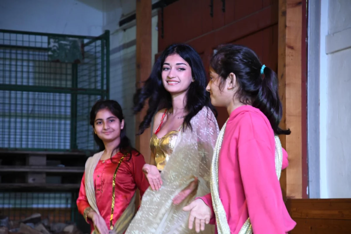 Three teenage girls in saris on a stage.