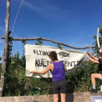 Two people attach a banner to tree trunks.