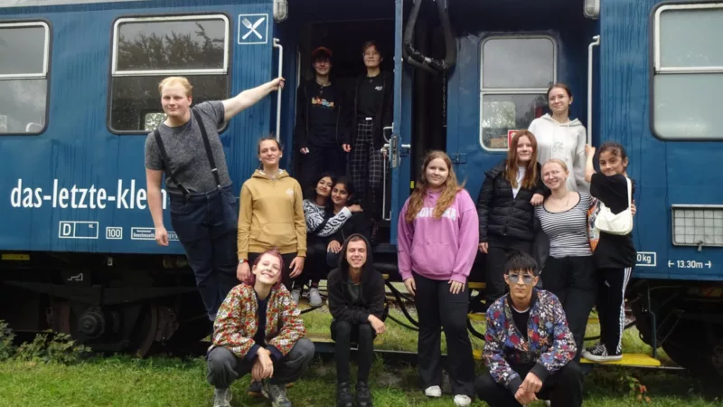 A group of young people pose in front of a blue train.